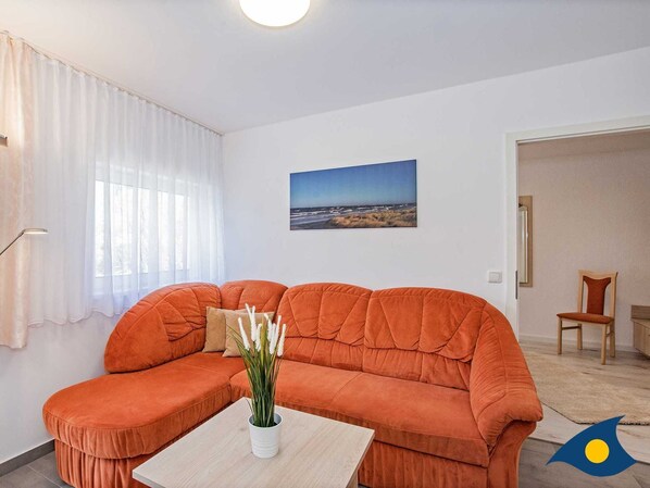Uma sala de estar com um sofá laranja grande, uma mesinha com uma planta e um quadro na parede.