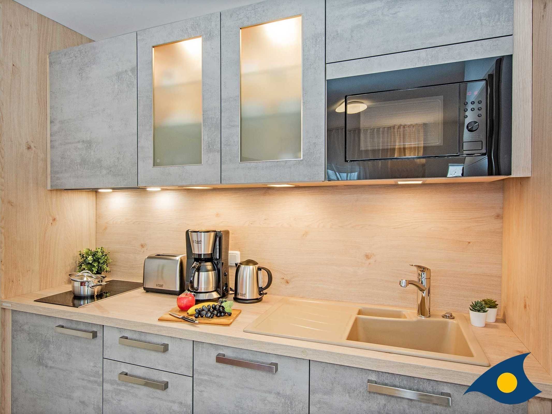 Een moderne keuken met grijze kastjes, een koffiezetapparaat van roestvrij staal, een magnetron en een spoelbak.