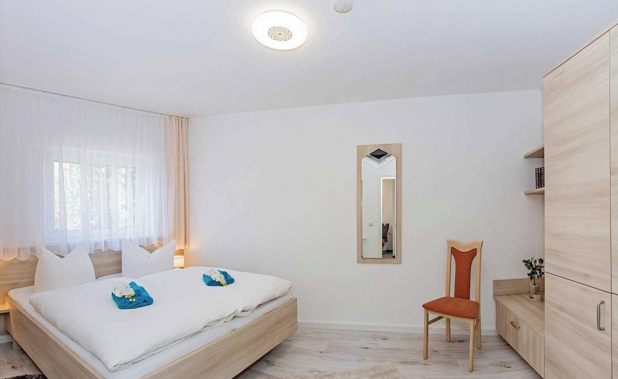 Ein Schlafzimmer mit Bett, Sessel, Kleiderschrank und Spiegel.