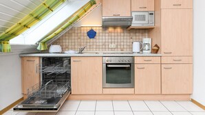A modern kitchen with wooden cabinets, a dishwasher, an oven, a microwave, and a skylight. - Apartment "Seediek" - Farm on the dike (Esens)