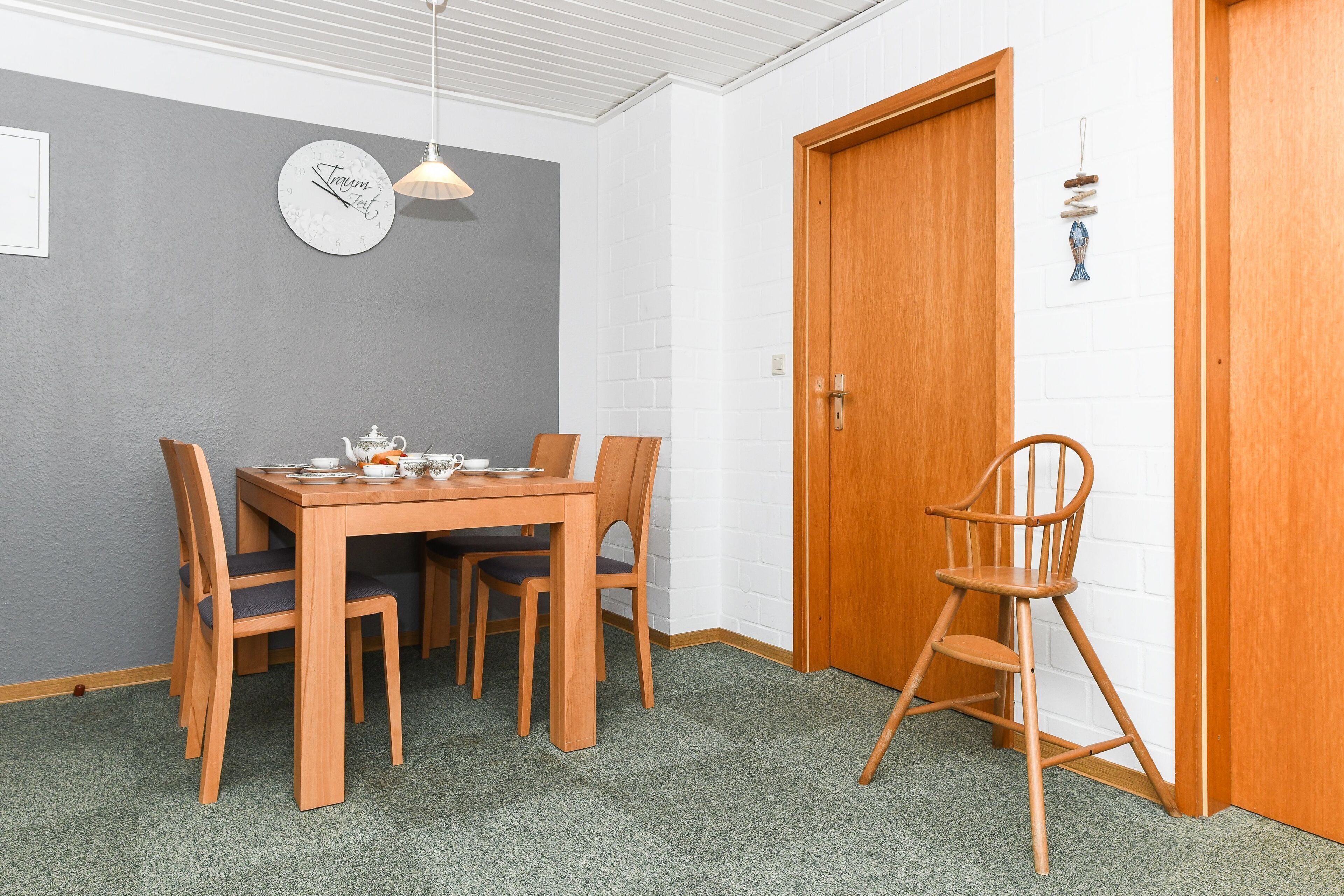 Een eethoek met een houten tafel en stoelen, een klok aan de muur en een deur met een decoratieve versiering.