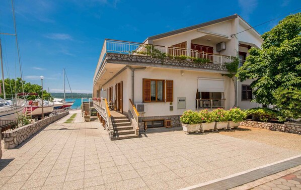 A two-story house with a balcony, a stone staircase, and a view of the sea.