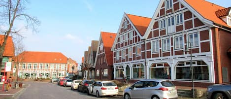 A cobblestone street lined with traditional half-timbered buildings, parked cars, and a clear sky.