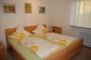 A double bed with floral bedding, a wooden headboard, and a bedside table with a lamp. There are three framed pictures on the wall above the bed.