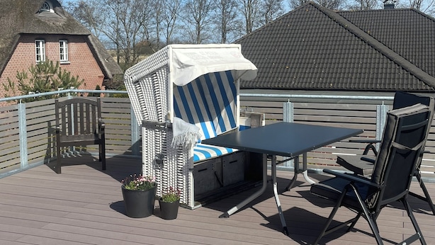 Une terrasse avec une table et des chaises, un espace salon couvert et une vue sur les bâtiments en arrière-plan.