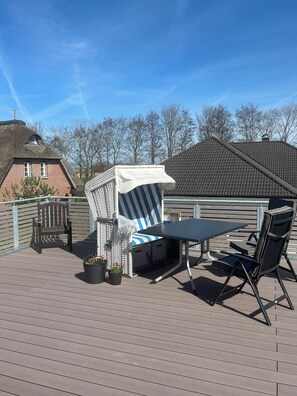 Une terrasse avec une table et des chaises, un espace salon couvert et une vue sur les bâtiments en arrière-plan.