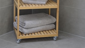 Une étagère en bois avec des serviettes pliées et des récipients blancs dans une salle de bain.