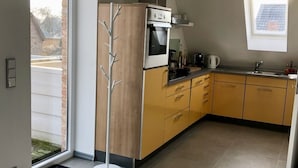 Une cuisine moderne équipée d’un four, d’un micro-ondes et d’une cuisinière encastrés. Elle comprend une grande fenêtre, un évier et un meuble en bois.