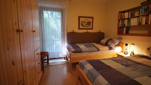 A bedroom with two single beds, a wooden wardrobe, a bedside table with a lamp, and a bookshelf.