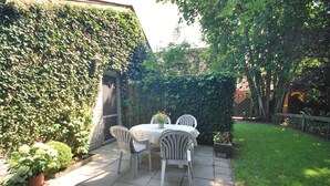 A patio with a table and chairs, surrounded by a garden and a wall covered in ivy.