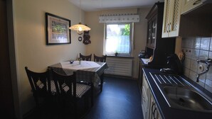A compact kitchen with a dining table, chairs, a hanging light fixture, a window with a curtain, and a built-in oven.