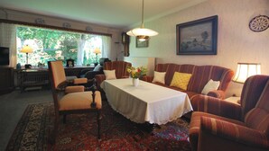 A traditional living room with a dining table, striped armchairs, a sofa, and a large window with a view of greenery.