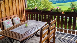 An outdoor wooden deck with a table and chairs, a decorative ceiling, and a view of a green landscape. - Cozy holiday apartment, surrounded by wood and grassland, chimney, pets allowed (Niedersachsen)