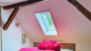 A bedroom with a sloped ceiling, a skylight, a wooden bed frame, and a small bedside table. - Cozy holiday apartment, surrounded by wood and grassland, chimney, pets allowed (Niedersachsen)