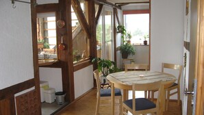 A cozy room with wooden beams, a round wooden table with chairs, a window with a view of greenery, and a door leading outside. - Cozy holiday apartment, surrounded by wood and grassland, chimney, pets allowed (Niedersachsen)