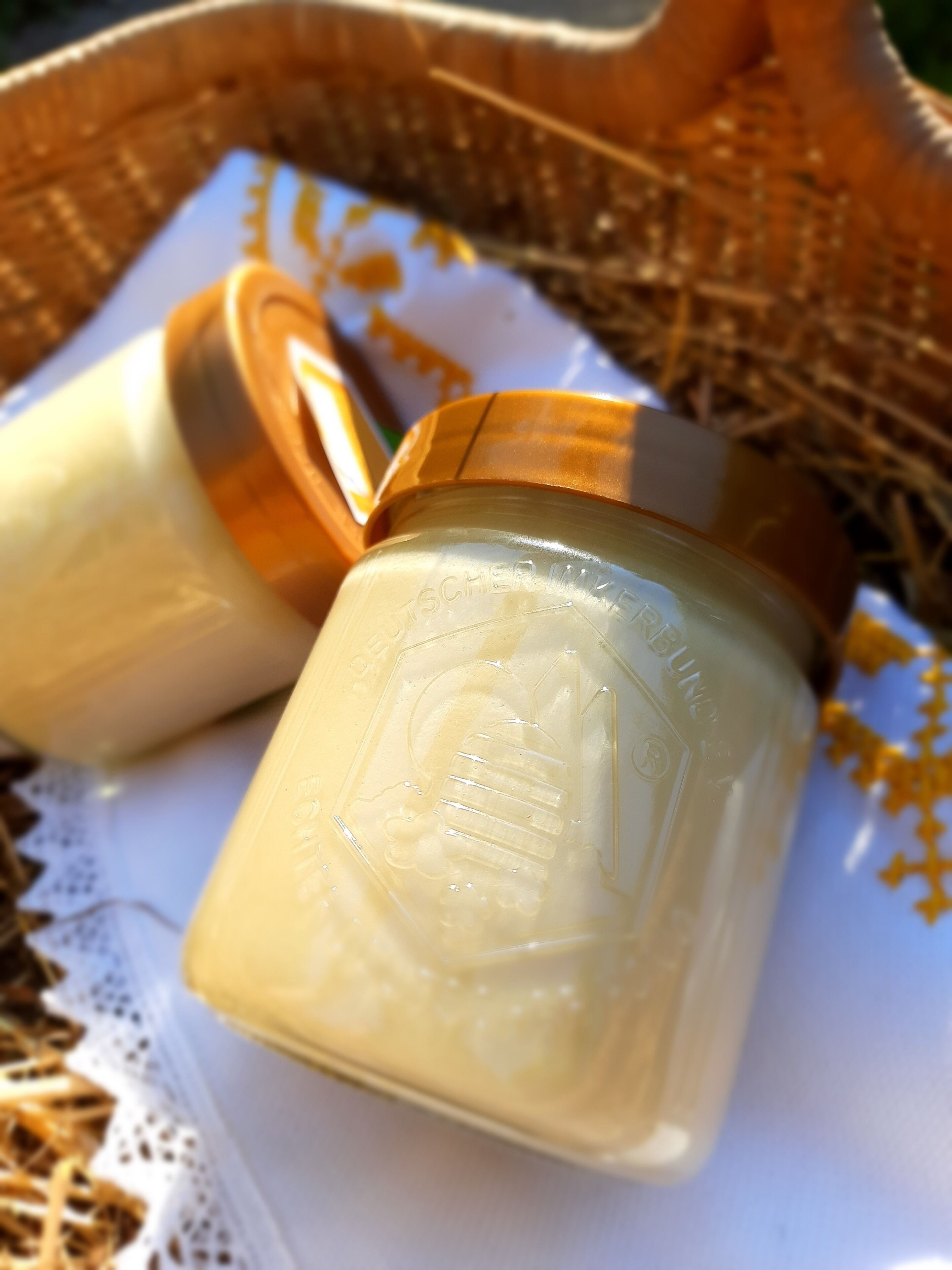 Two honey jars with embossed labels in a wicker basket.
