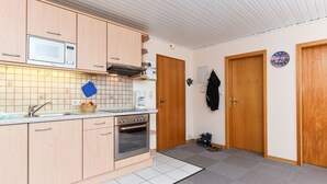 Ett kompakt kök med mikrovågsugn, ugn och diskho. Köket har träskåp och en kakelbeklädd vägg bakom diskbänken.
