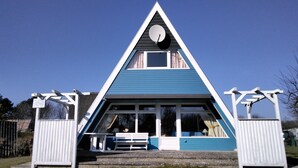 A triangular building with a blue roof and white walls, featuring a large window and a door. - Sunny, cozy wooden holiday house with big terrace and BBQ (Schleswig-Holstein)