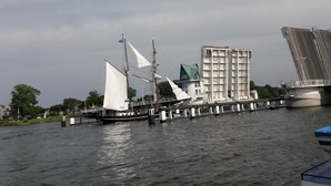 A river with a sailboat docked near a building with a green roof and a bridge in the background. - Sunny, cozy wooden holiday house with big terrace and BBQ (Schleswig-Holstein)
