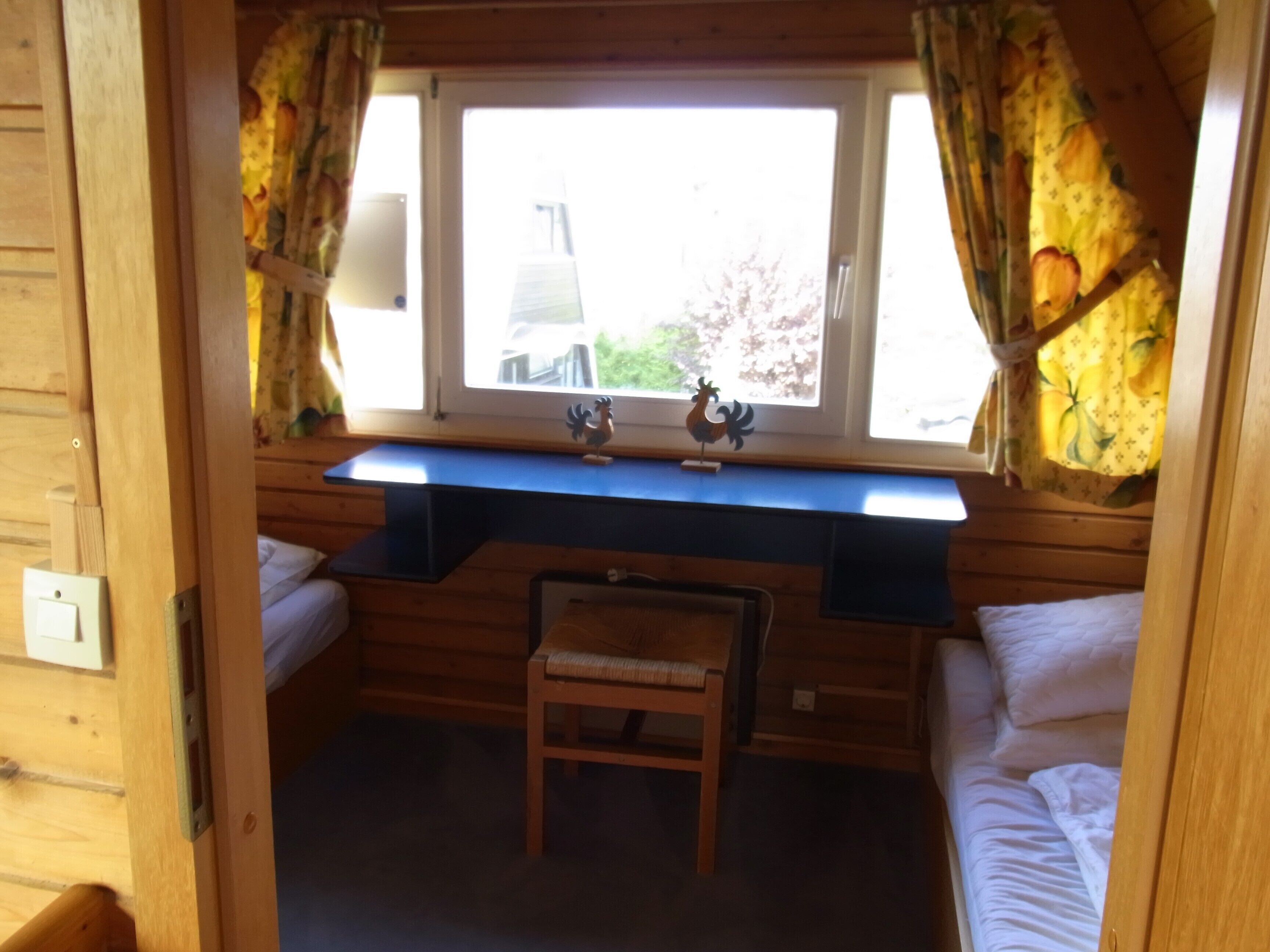 Eine kleine Holzhütte mit Holzausstattung, einem Fenster mit Vorhängen, einem Schreibtisch mit einem Hahn als Dekoration und zwei Betten.