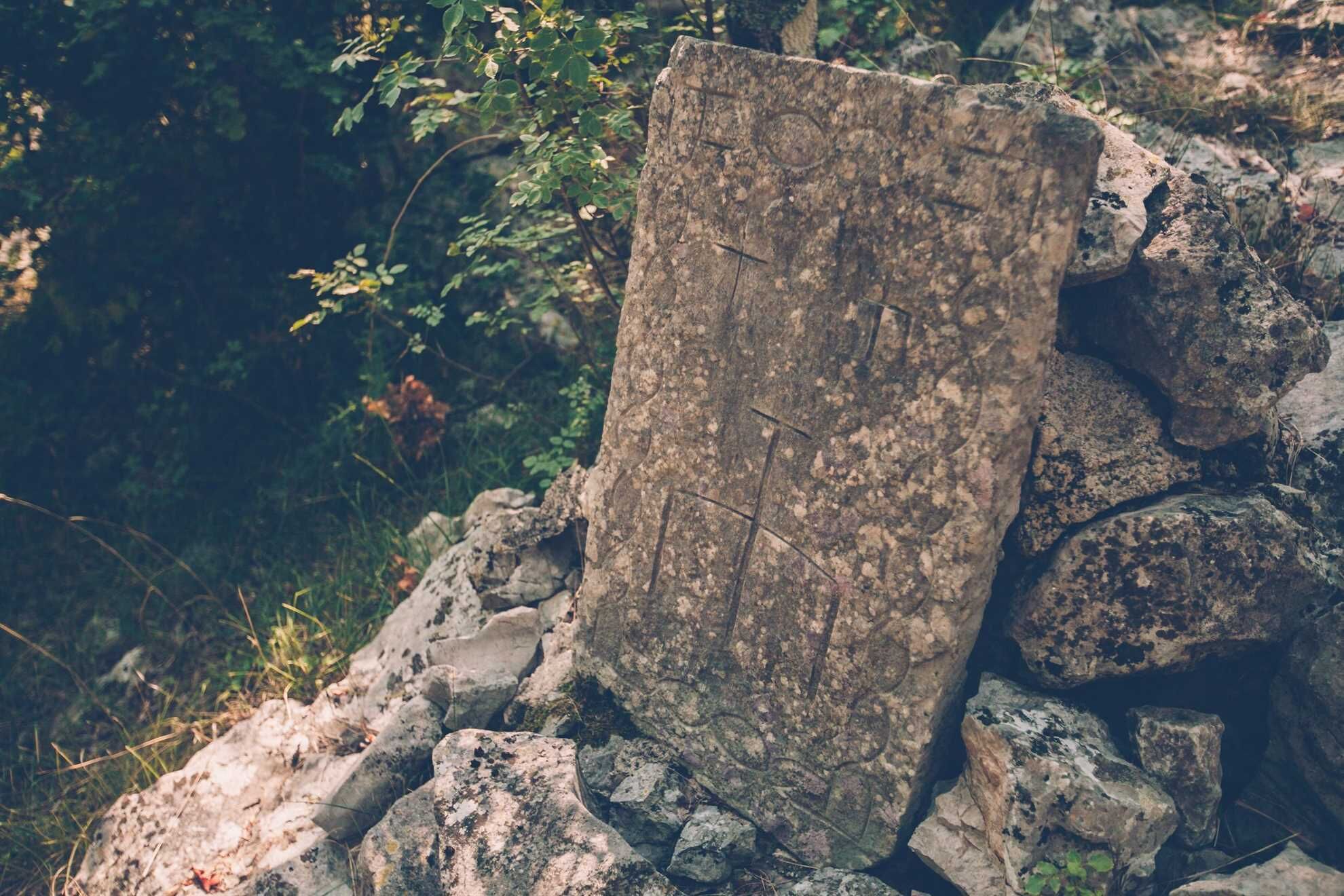 A large, weathered stone slab with visible carvings, surrounded by rocks and foliage.