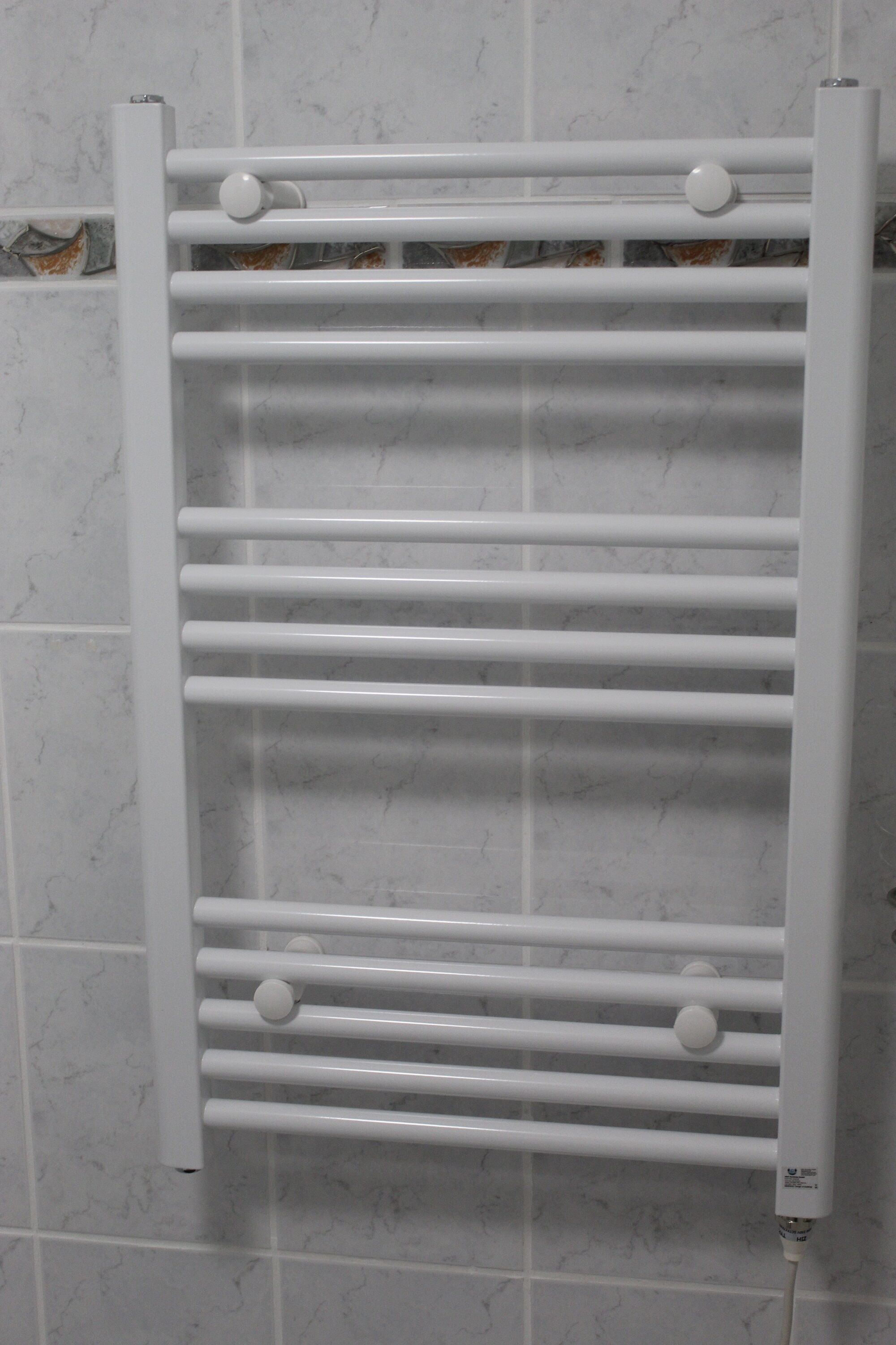 Un porte-serviettes blanc, doté de plusieurs barres horizontales et de boutons ronds, fixé à un mur carrelé.