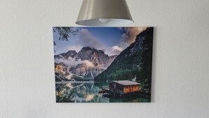Een eetruimte met een tafel, stoelen, een lamp en een lijst met een berglandschap.