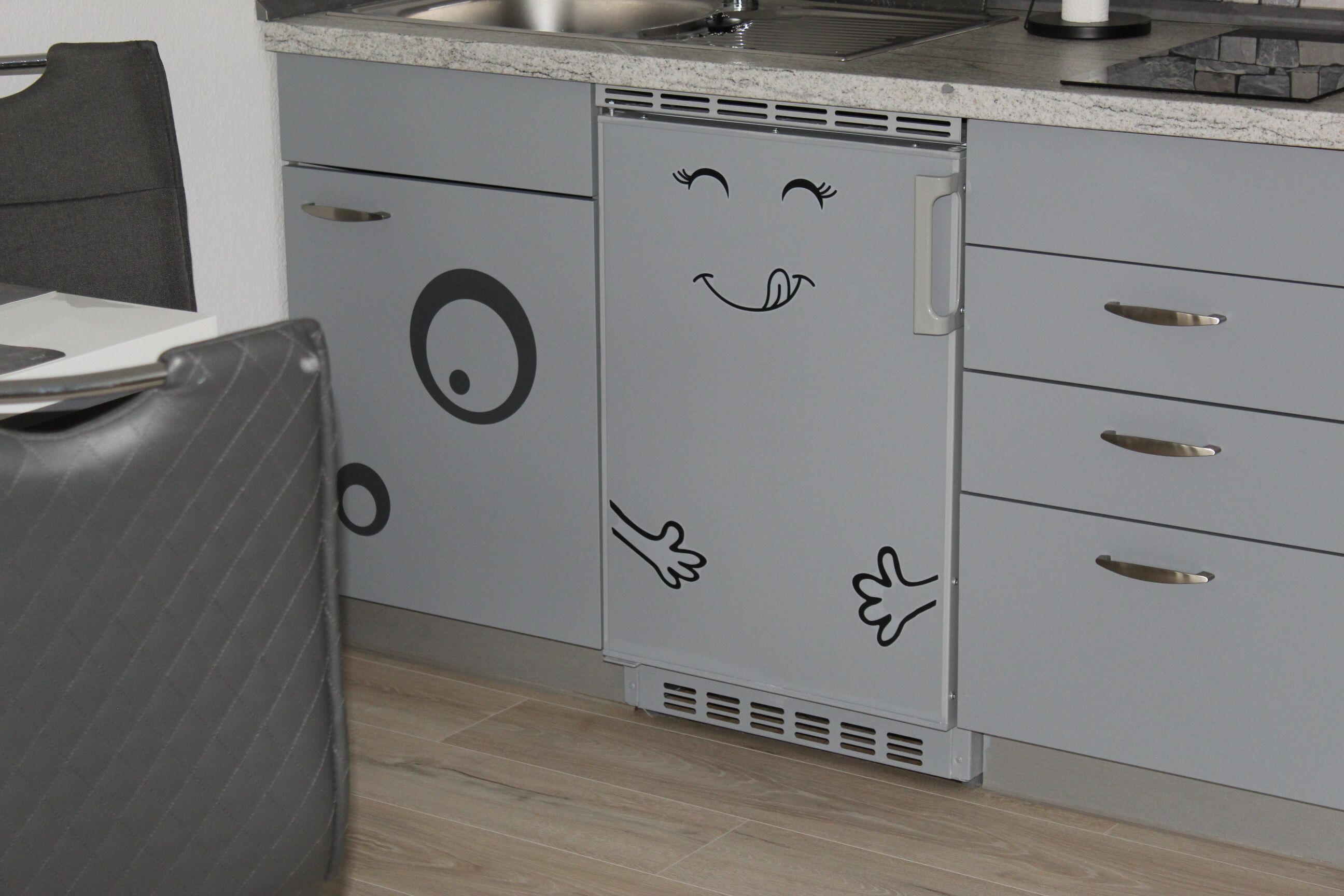 Une cuisine avec des meubles gris ornés d’un motif représentant un visage souriant.