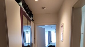 Een gang met houten vloer, een garderobe en een bed op de achtergrond.
