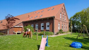 Ein Backsteinhaus mit rotem Ziegeldach, ein Spielplatz mit Rutsche und Schaukeln.