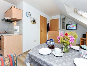 A compact kitchen with a microwave, kettle, and a dining table set with plates and a cup.
