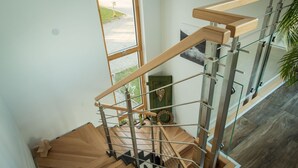 A modern staircase with wooden steps and glass railings, leading to a second floor with a view of the outdoors. - Apartment in an idyllic location and great views (Dormettingen)