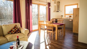 A cozy living room with a sofa, a dining table, and chairs. There is a kitchen area with a stove and cabinets. Large windows allow natural light to fill the space. - Apartment in an idyllic location and great views (Dormettingen)