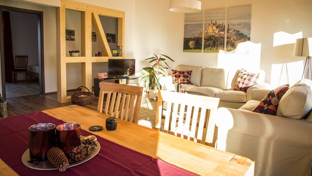 A cozy living room with a wooden dining table, a sofa, and a TV. There's a bookshelf and a plant in the room. - Apartment in an idyllic location and great views (Dormettingen)