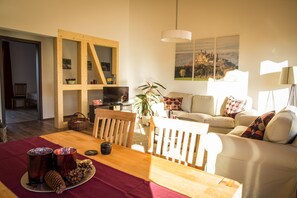 A cozy living room with a wooden dining table, a sofa, and a TV. There's a bookshelf and a plant in the room. - Apartment in an idyllic location and great views (Dormettingen)