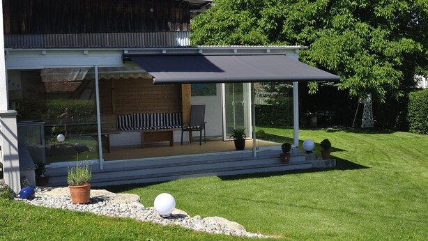 A modern house with a covered patio, a bench, and potted plants. - Ground floor apartment (Neukirch)