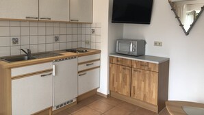A compact kitchen with a built-in microwave, a sink, and wooden cabinets. - Ground floor apartment (Neukirch)