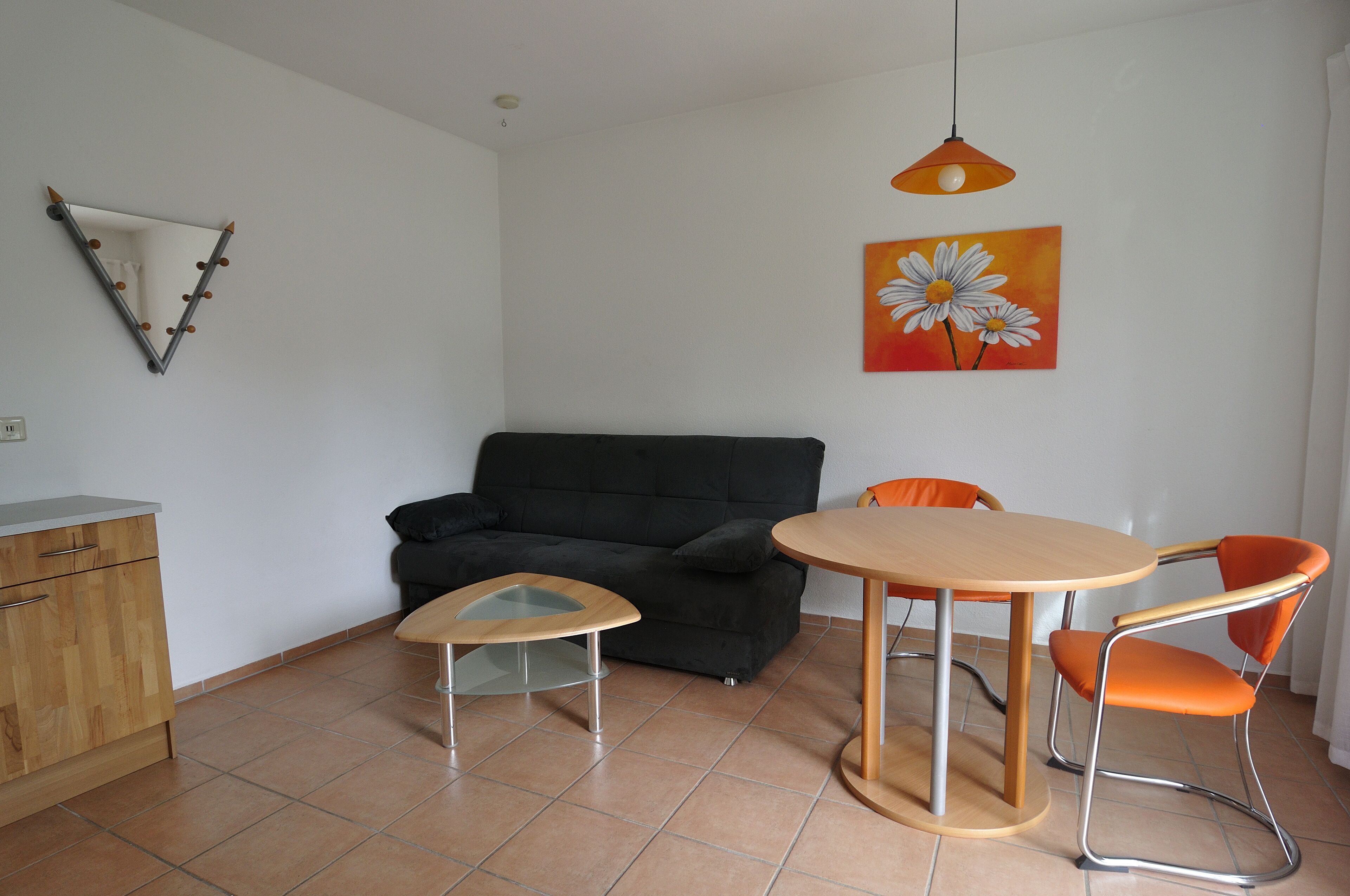 A compact living space with a black sofa, a small round table, and two orange chairs.