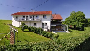A two-story house with a red-tiled roof, a balcony, and a covered porch. - Ground floor apartment (Neukirch)