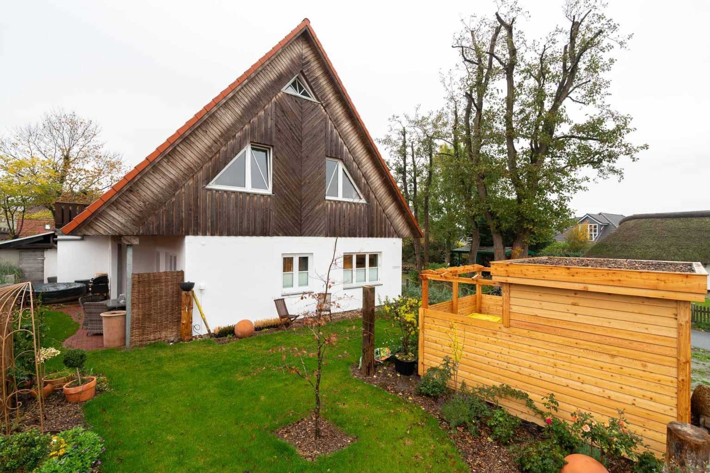 A house with a triangular roof, white exterior walls, and a small garden with a wooden structure.