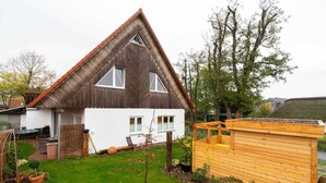 A house with a triangular roof, white exterior walls, and a small garden with a wooden structure.