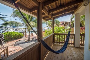 A wooden deck with a hammock, palm trees, and a view of boats on the water.