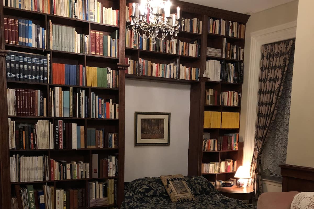 A cozy room with a large bookshelf filled with books, a comfortable bed, a chair, and a desk.