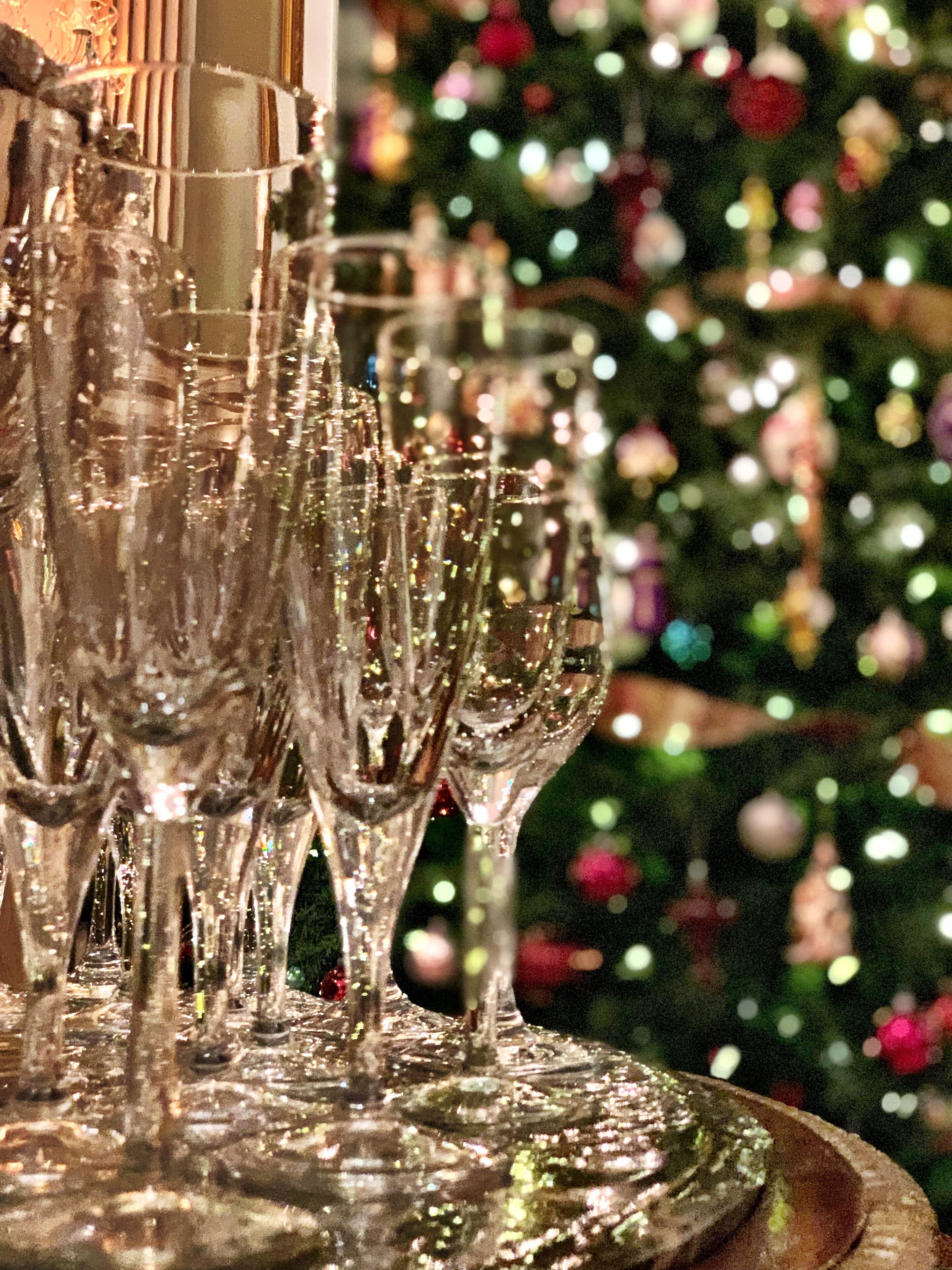 A row of empty champagne flutes on a table, with a blurred Christmas tree in the background.