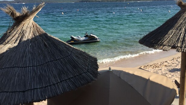 Ein Strand mit Reetdachschirmen und einem Jetski im Wasser.