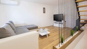 A modern living room with a sofa, a glass coffee table, a TV, and a staircase with a railing. - Holiday home With terrace and whirlpool (Medulin)