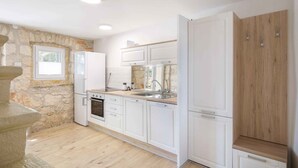 A modern kitchen with white cabinets, a stone accent wall, a built-in oven, and a wooden cabinet. - Holiday home With terrace and whirlpool (Medulin)
