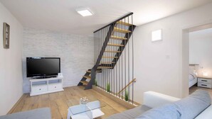 A modern living room with a staircase, a flat-screen TV, a glass coffee table, and a grey sofa. - Holiday home With terrace and whirlpool (Medulin)