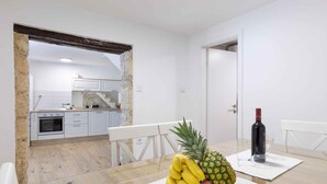 A modern kitchen with white cabinets, a dining table with a fruit bowl, and a wine bottle. - Holiday home With terrace and whirlpool (Medulin)