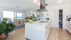 Eine moderne Küche mit einer zentralen Kochinsel, einem Essbereich mit Stühlen und Blick ins Freie.